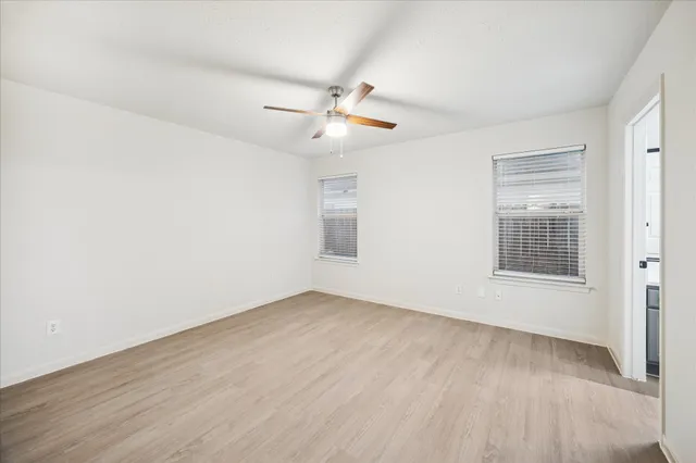 an empty room with wooden floor ceiling fan and windows