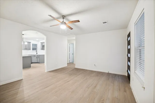 an empty room with wooden floor a ceiling fan and windows