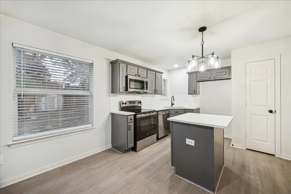 a kitchen with stainless steel appliances granite countertop a stove top oven a sink dishwasher a refrigerator and a dining table with wooden floor