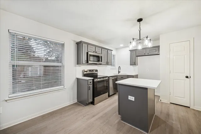 a kitchen with stainless steel appliances granite countertop a stove top oven a sink dishwasher a refrigerator and a dining table with wooden floor