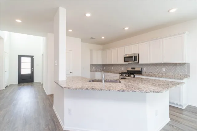 a kitchen with stainless steel appliances granite countertop a sink dishwasher a stove and a refrigerator with wooden floor