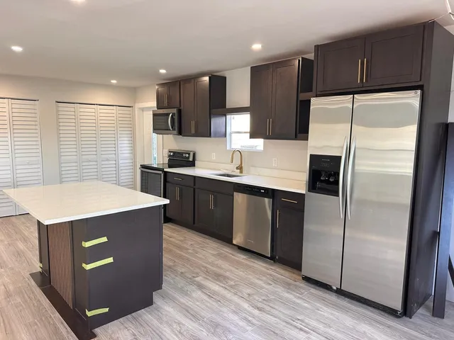 a kitchen with stainless steel appliances granite countertop a refrigerator a sink a stove a microwave a counter space and wooden floor