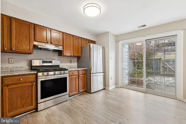 a kitchen with stainless steel appliances granite countertop a stove a refrigerator and a sink with wooden cabinets