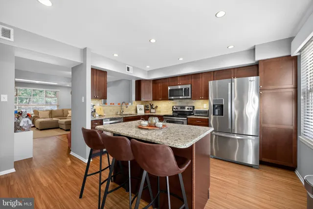 a kitchen with stainless steel appliances granite countertop a refrigerator a stove a sink a dining table and chairs with wooden floor