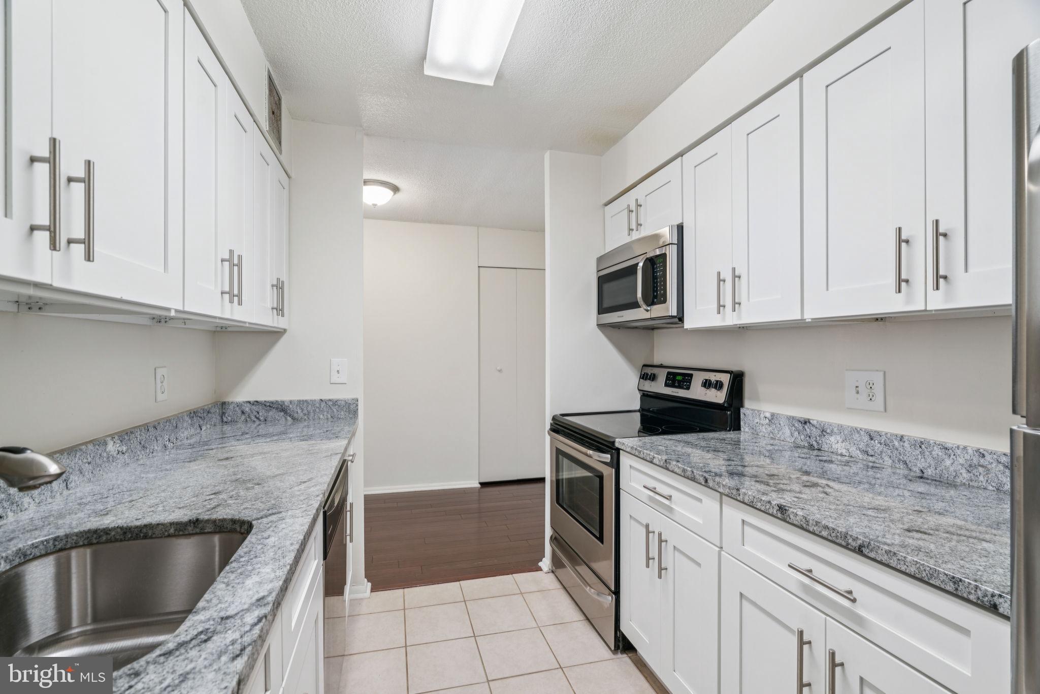 1420 Locust Street, Unit 28P Philadelphia, PA 19102 - Photo 9 of 25 a kitchen with granite countertop a sink dishwasher stove and microwave with wooden cabinets