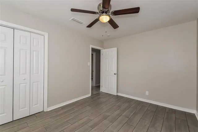 an empty room with wooden floor fan and windows