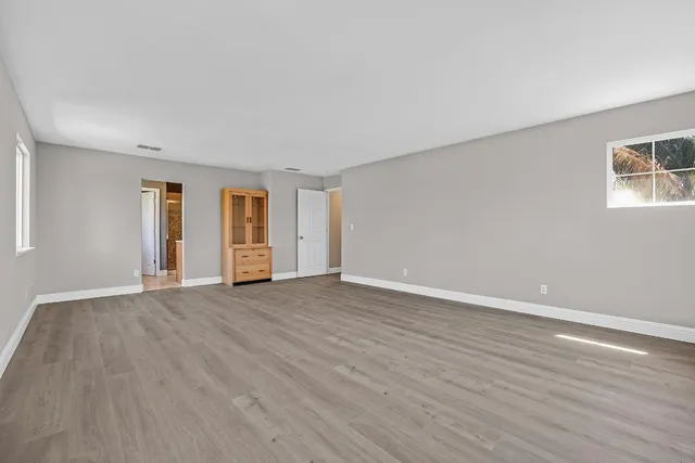 a view of an empty room with wooden floor and window
