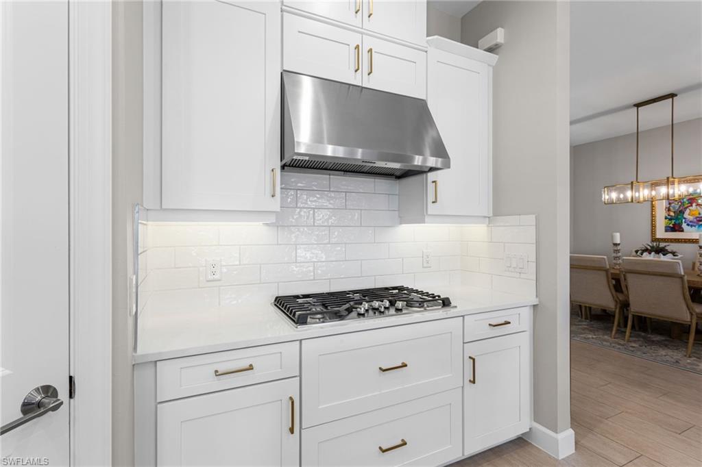 15216 Turin Drive Naples, FL 34114 - Photo 10 of 50 Kitchen with white cabinets, decorative backsplash, light stone countertops, and light wood finished floors