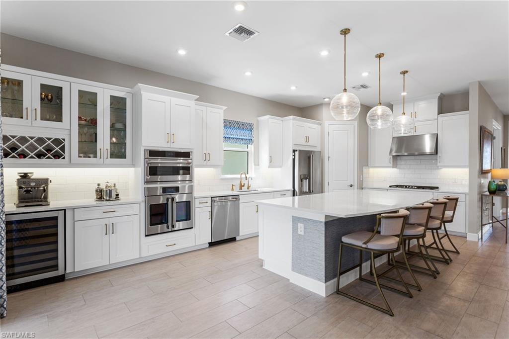 15216 Turin Drive Naples, FL 34114 - Photo 5 of 50 Kitchen with wine cooler, a kitchen bar, white cabinets, hanging light fixtures, and stainless steel appliances
