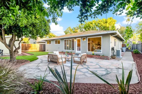 a view of a backyard with table and chairs potted plants and large tree