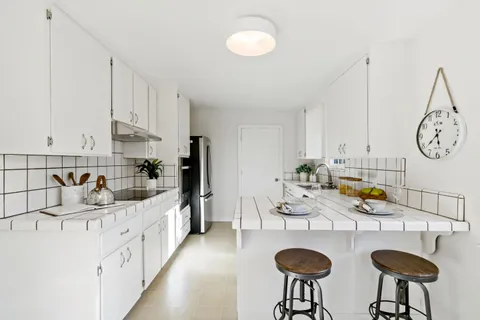 a kitchen with stainless steel appliances granite countertop a sink a stove white cabinets with chairs and couches