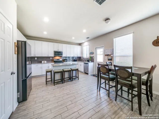 a kitchen with stainless steel appliances kitchen island granite countertop a table chairs and a refrigerator