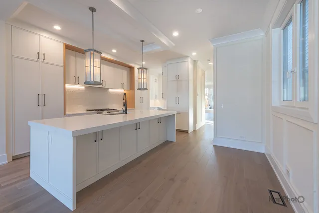 a large white kitchen with a refrigerator a sink dishwasher a stove and white cabinets with wooden floor