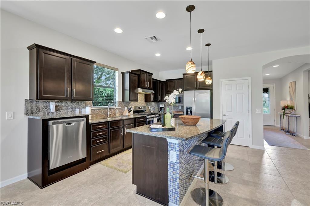7103 Lily Way Naples, FL 34114 - Photo 7 of 41 a kitchen with stainless steel appliances kitchen island granite countertop a sink dishwasher a stove a refrigerator with a dining table and chairs