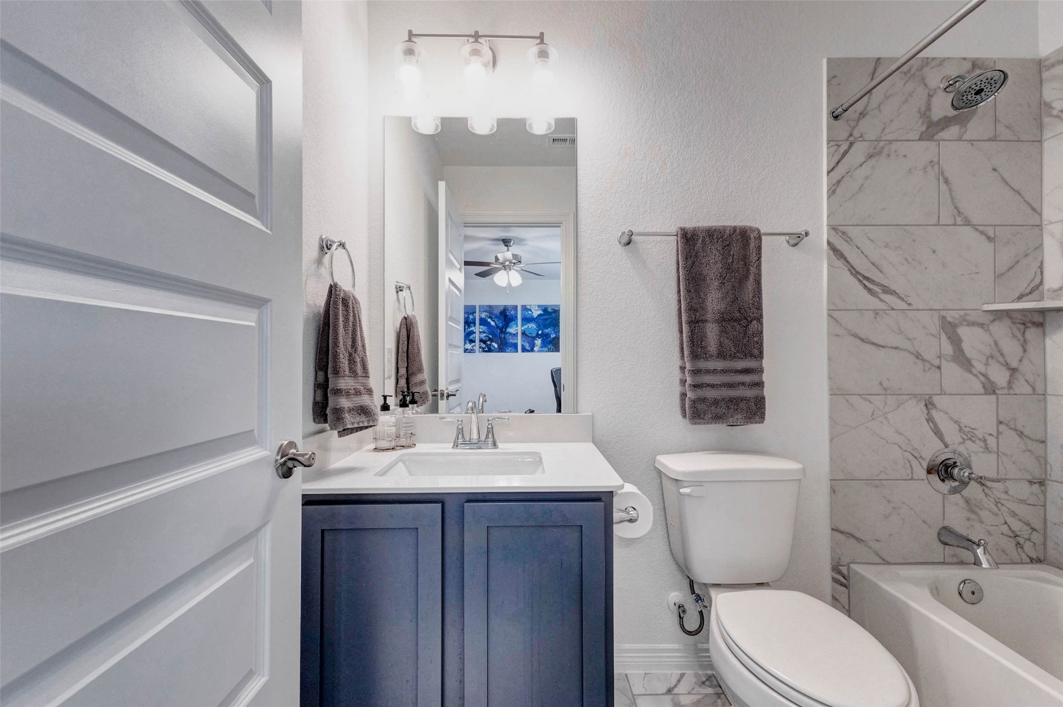 32418 Fly Fish Way Fulshear, TX 77441 - Photo 30 of 40 The full guest bathroom is beautifully appointed with the same bold blue cabinetry and crisp white countertop found throughout the home, complemented by upgraded lighting fixtures and a tub and shower combination with a stunning marbled look tile surround.