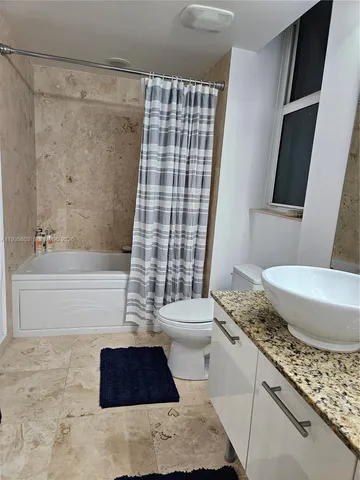a bathroom with a granite countertop bathtub shower sink vanity and toilet