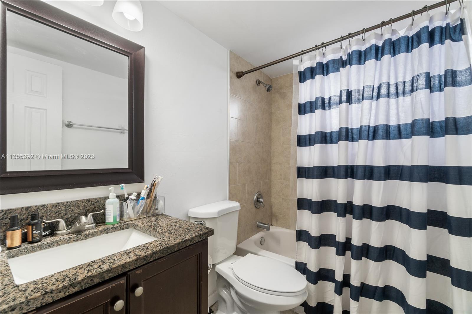 14140 Southwest 84th Street, Unit 208H Miami, FL 33183 - Photo 8 of 29 a bathroom with a granite countertop sink a toilet a mirror a lamp and shower curtain