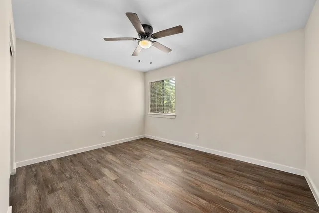 an empty room with wooden floor fan and windows