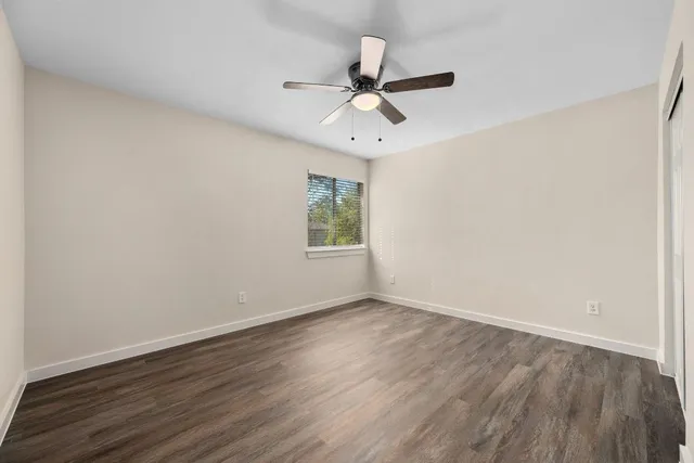 an empty room with wooden floor ceiling fan and windows
