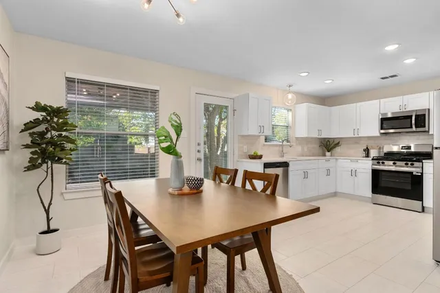 a kitchen with stainless steel appliances kitchen island granite countertop a dining table chairs and white cabinets