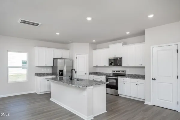 a kitchen with stainless steel appliances granite countertop a stove top oven a sink a refrigerator and white cabinets with wooden floor