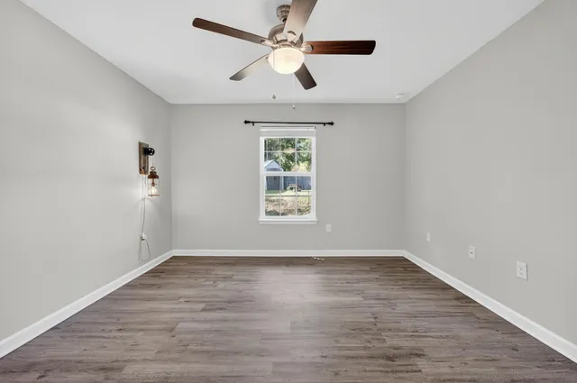 an empty room with wooden floor ceiling fan and windows