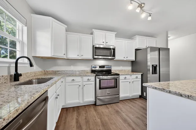 a kitchen with stainless steel appliances granite countertop a stove top oven a refrigerator a sink and dishwasher with wooden floor