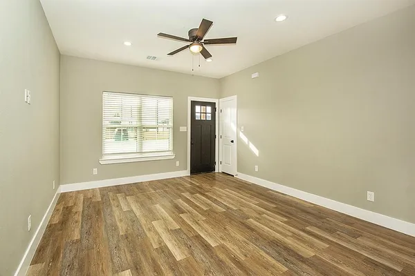 an empty room with wooden floor ceiling fan and windows