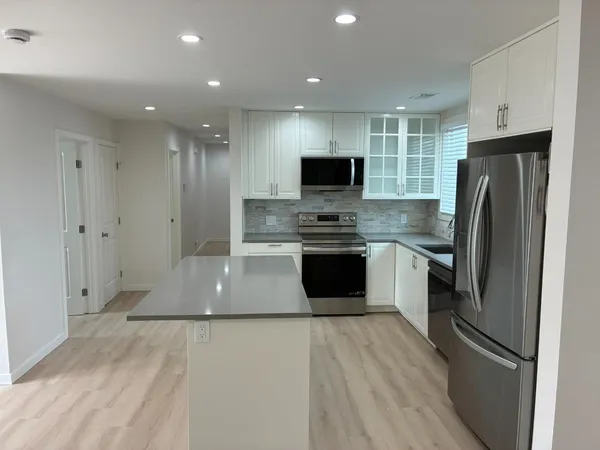 a large kitchen with stainless steel appliances granite countertop a refrigerator a sink dishwasher a stove and a refrigerator with wooden floor