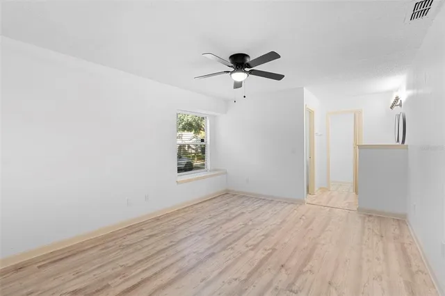 a view of empty room with wooden floor and fan