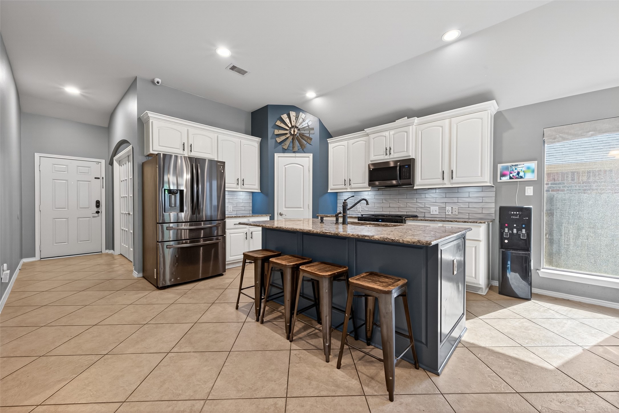 27443 Rebecca Field Lane Spring, TX 77386 - Photo 10 of 31 This kitchen features modern stainless steel appliances, a central island with bar stools, and stylish white cabinetry. The tile flooring and neutral wall colors create a bright, inviting space perfect for cooking and entertaining.
