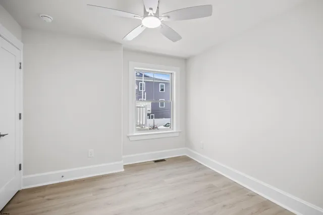 an empty room with wooden floor chandelier fan and windows