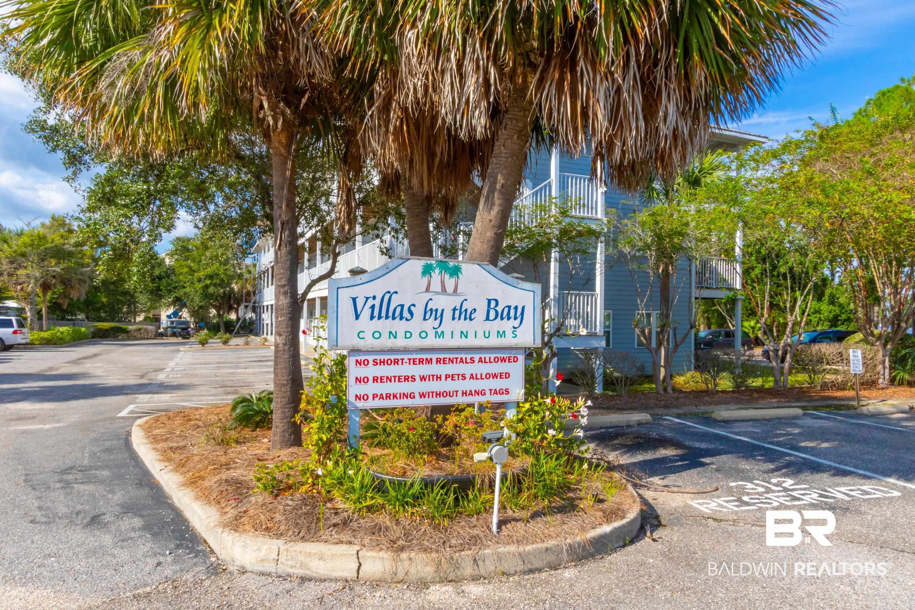 25957 Canal Road, Unit 208 Orange Beach, AL 36561 - Photo 28 of 28 Entryway signage for "Villas by the Bay Condominiums" with a light blue building exterior featuring white railings