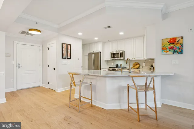 a kitchen with stainless steel appliances granite countertop a stove a sink a microwave a refrigerator and white cabinets with wooden floor