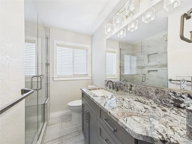 a bathroom with a granite countertop sink a toilet a mirror and shower
