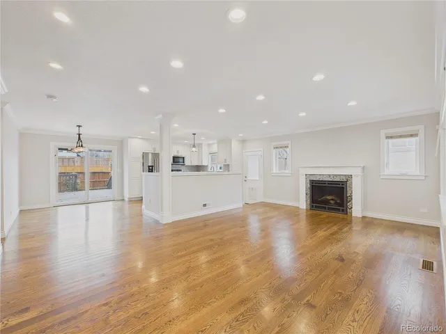a view of an empty room with wooden floor and a kitchen