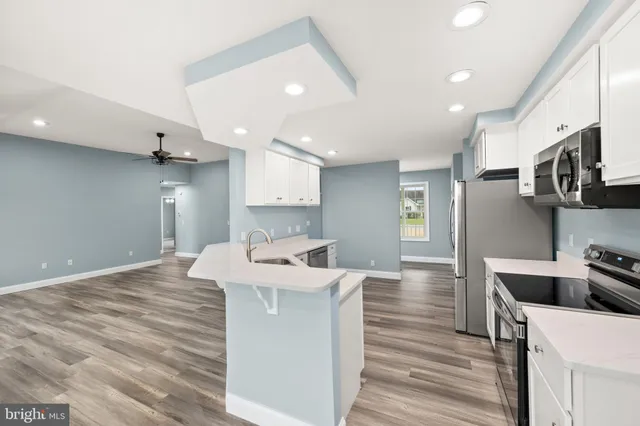 a large kitchen with stainless steel appliances kitchen island a stove a refrigerator a oven and white cabinets with wooden floor