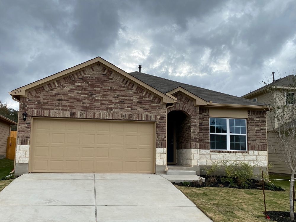 6713 Ranchito Drive Austin, TX 78744 - Photo 2 of 12 View of front of house featuring an attached garage, brick siding, stone siding, driveway, and roof with shingles