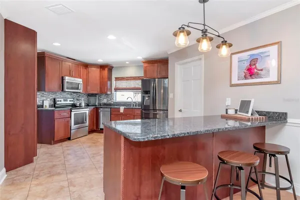 a kitchen with stainless steel appliances granite countertop a stove a sink a microwave a refrigerator and chairs