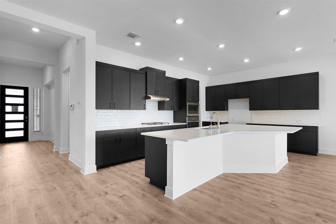 1129 Pansy Trail Georgetown, TX 78628 - Photo 7 of 28 a large white kitchen with kitchen island a sink a center island stainless steel appliances and a couch
