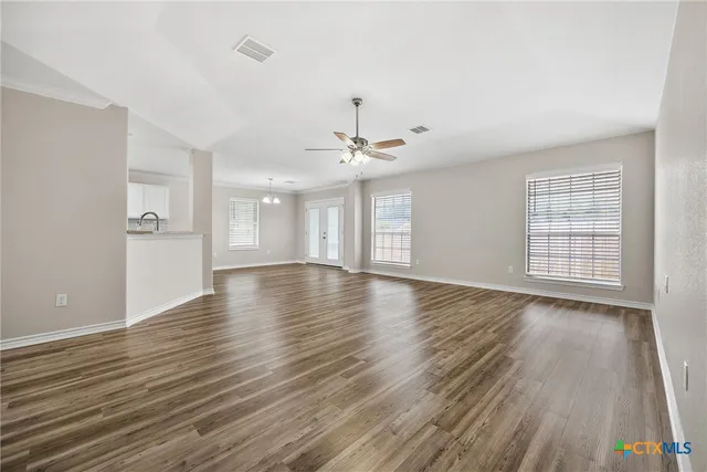 an empty room with wooden floor chandelier and windows
