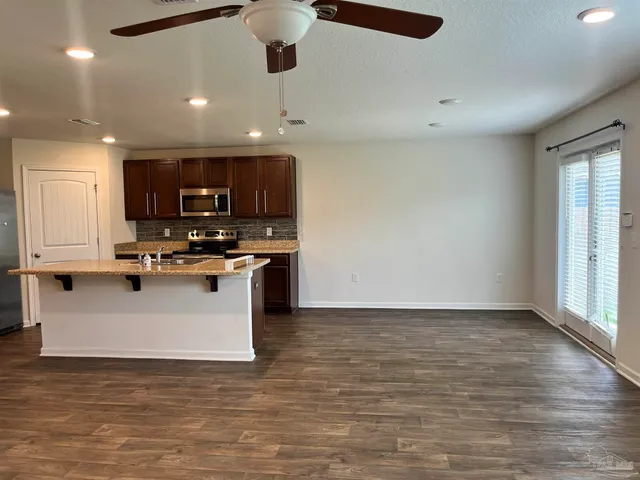 a view of kitchen with stainless steel appliances granite countertop a stove top oven a sink a refrigerator and white cabinets with wooden floor