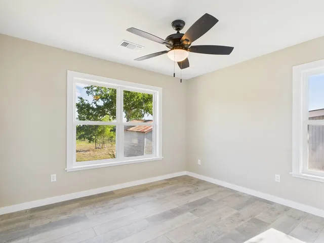 an empty room with wooden floor fan and windows