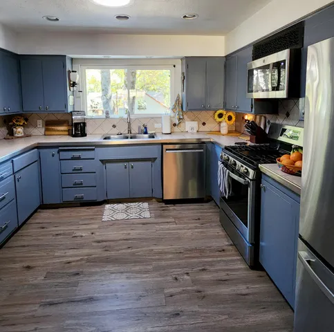a kitchen with stainless steel appliances granite countertop a stove a sink dishwasher and a refrigerator with wooden floor