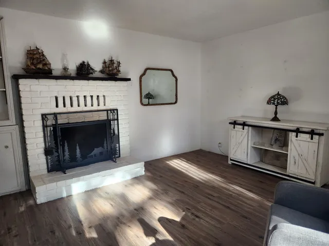 a view of an empty room with wooden floor fireplace and a window