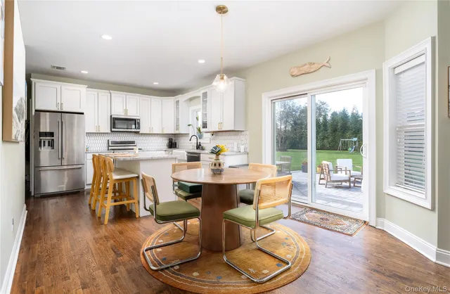 a dining room with stainless steel appliances kitchen island granite countertop a refrigerator a stove a sink dishwasher a dining table and chairs with wooden floor