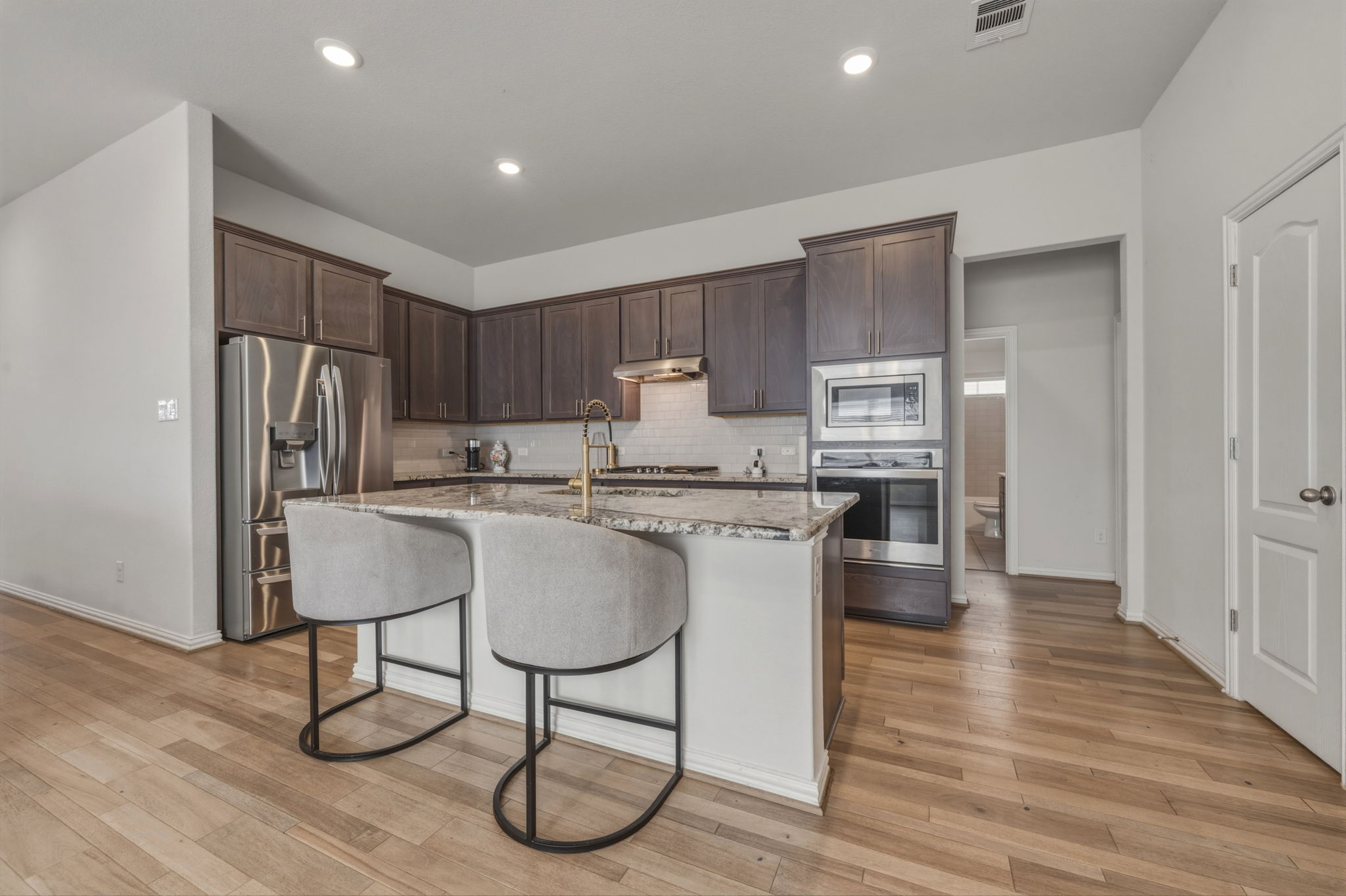 918 Leadtree Loop Buda, TX 78610 - Photo 6 of 27 Kitchen featuring dark wood finish cabinets, stainless steel appliances, light stone countertops, an island with sink, and light wood-style flooring