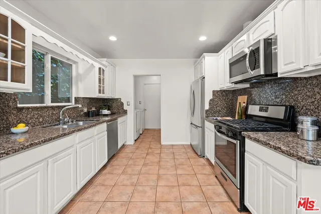 a large kitchen with stainless steel appliances granite countertop a stove top oven a sink a counter space and cabinets