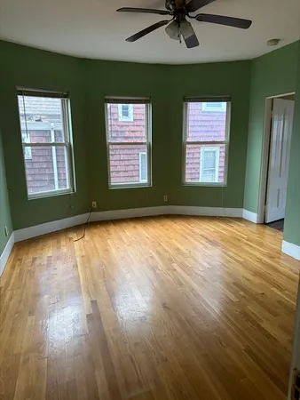 an empty room with wooden floor a ceiling fan and windows