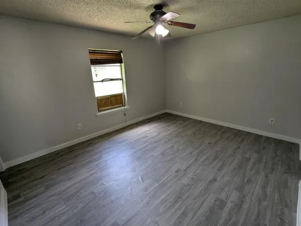 an empty room with wooden floor chandelier fan and windows